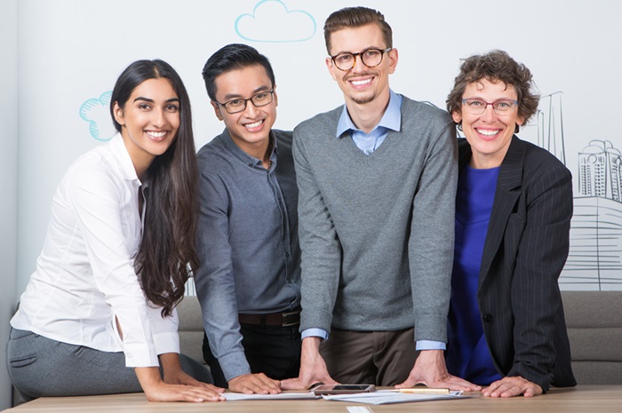 four smiling business people standing table